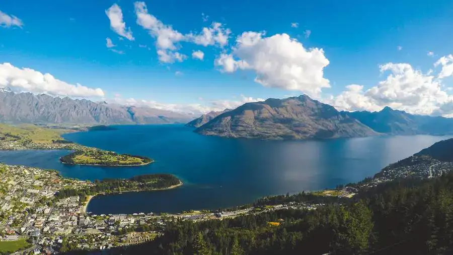 View over Queenstown to Lake Wakatipu and surrounding mountains on a sunny day..