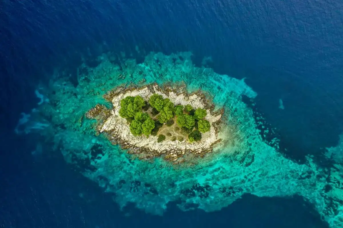 Trees on a tiny islet surrounded by turquoise Adriatic Sea in Croatia.