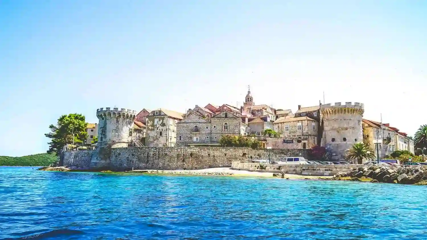 Blue sea fronts fortified walls and turrets of Korčula Island.