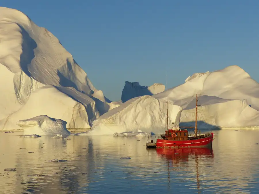 A red ship sails between the giant icebergs off Ilulissat in the midnight sun.