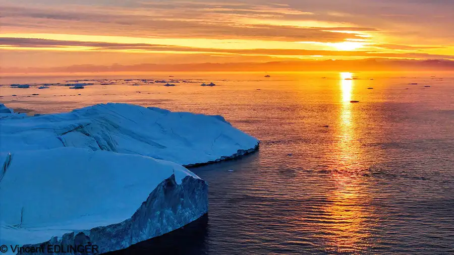 The midnight sun shines goldenly over icebergs in the sea near Ilulissat.