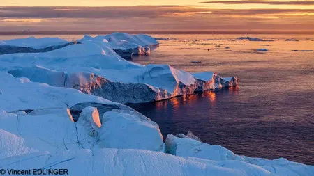 This image captures the serene beauty of the midnight sun over Greenland’s icy terrains.