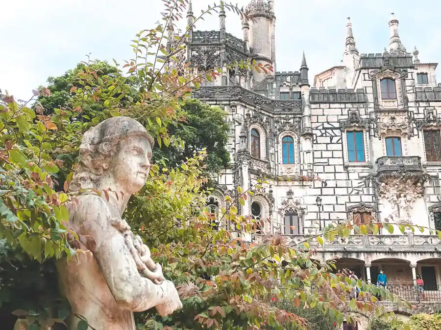 Statue in foliage in front of a gothic mansion.