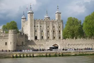 The tower of London castle and battlements seen from the Thames river.