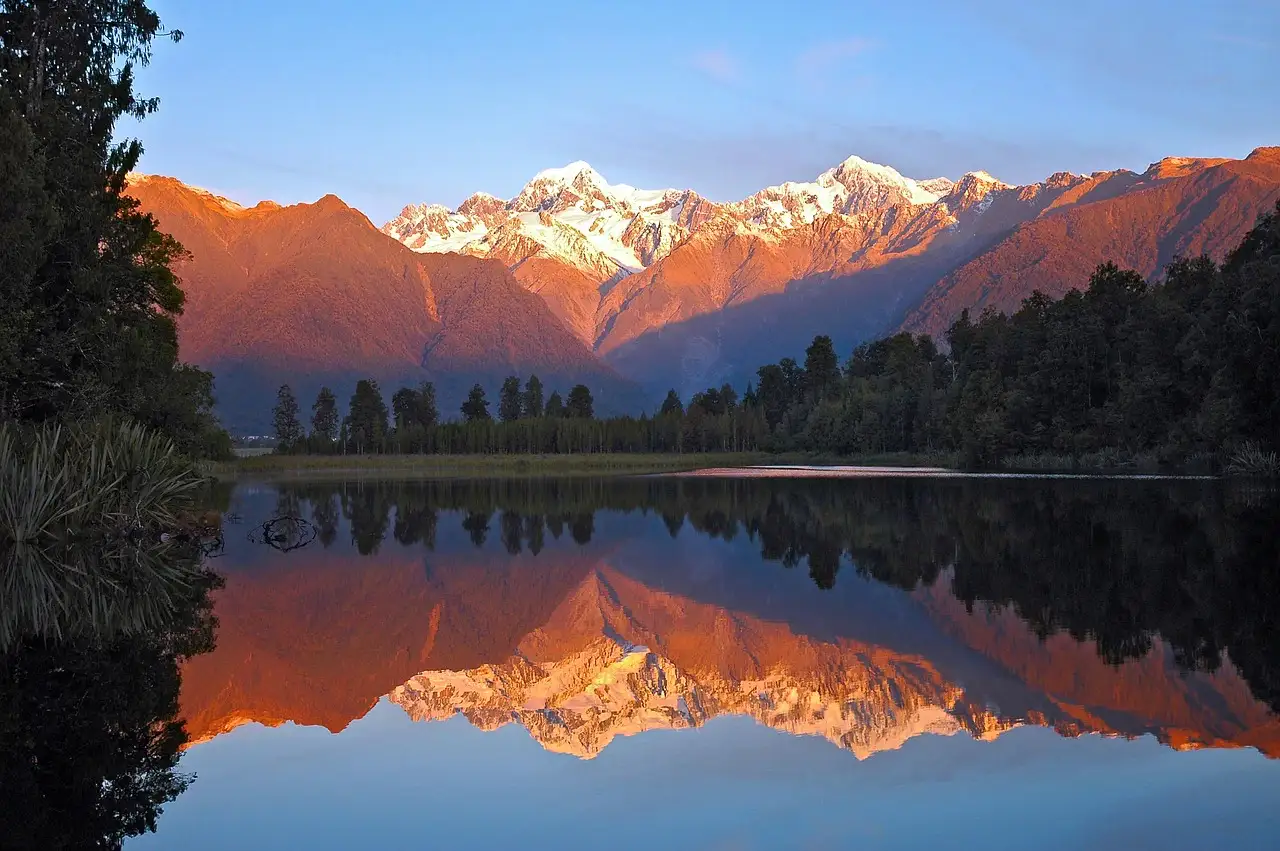 Orange reflection at sunrise of snowy mountains on a lake.