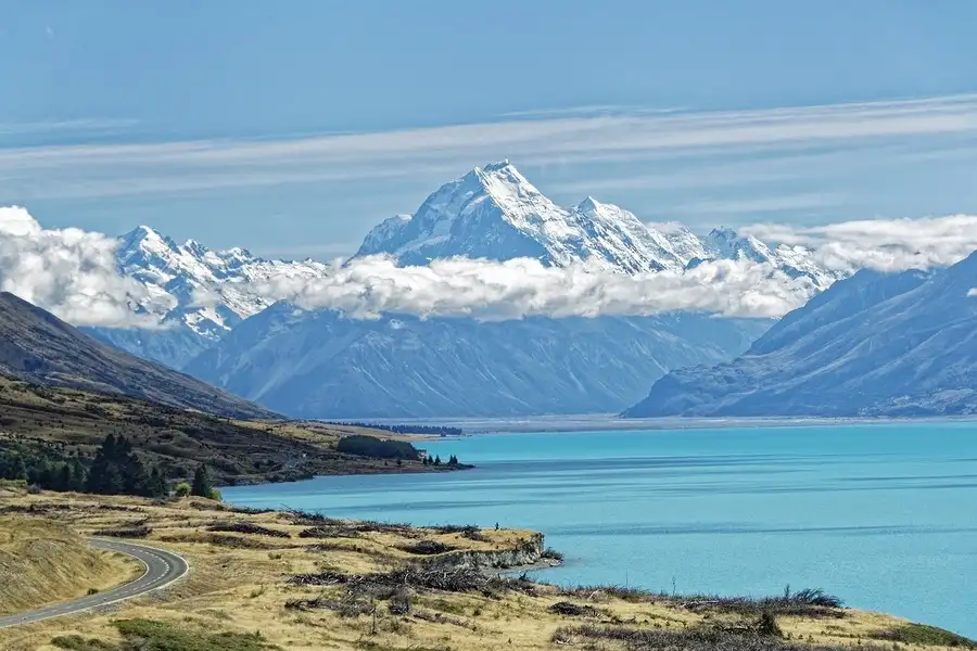 Road beside blue Pukaki lake with snowy Mount Cook in the distance.