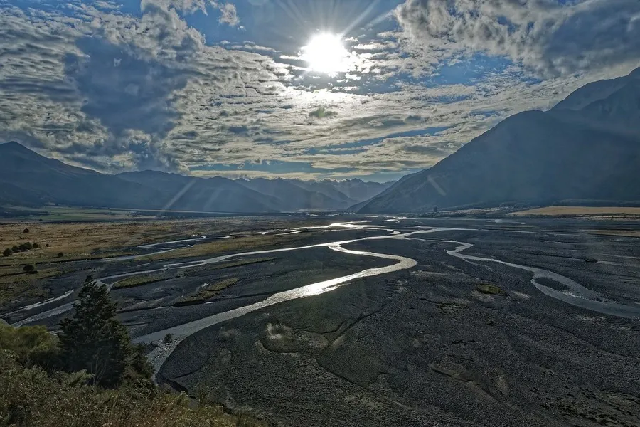 Sun through the clouds over Arthur's Pass, rivers in a mountain valley.