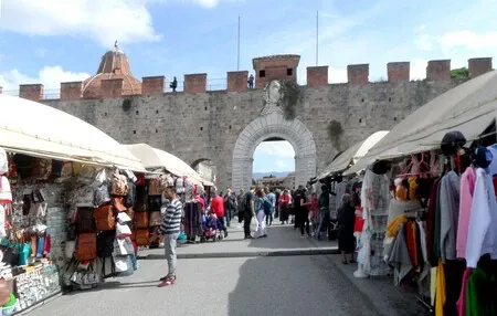Street market stalls in front of an arch gateway in a medieval wall.