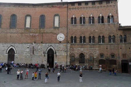 Visitors walking outside the brick façade of Santa Maria della Scala in Siena.