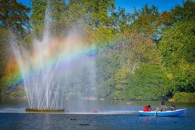 Family in a rowing boat by a fountain on the river in Hyde Park.