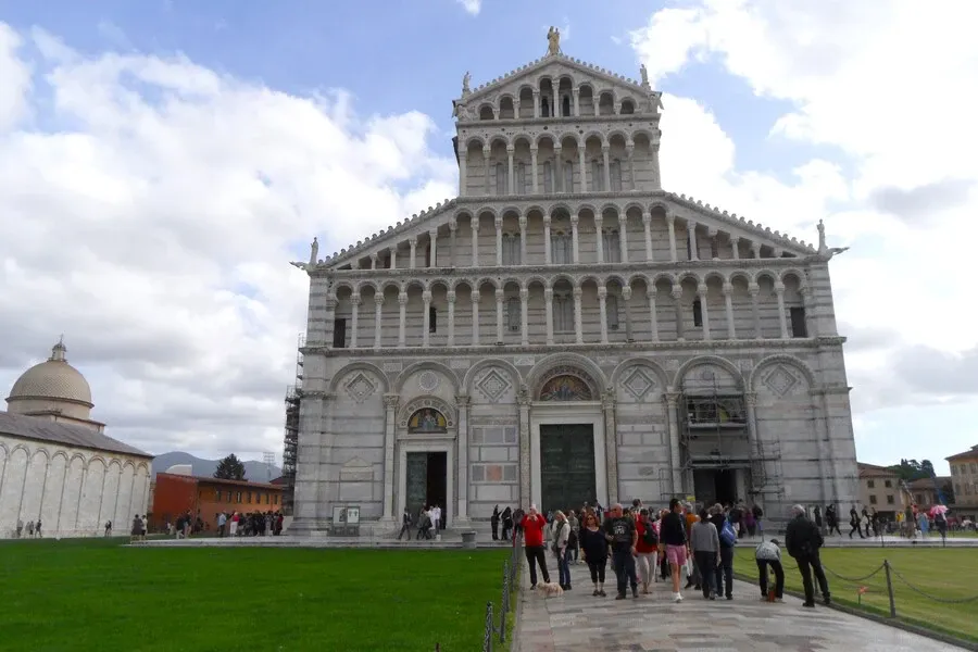 Pisa cathedral colonnaded façade made of white marble with visitors outside.